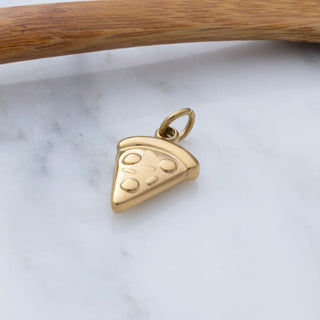 Gold pizza slice pendant on a marble surface with a wooden stick in the background
