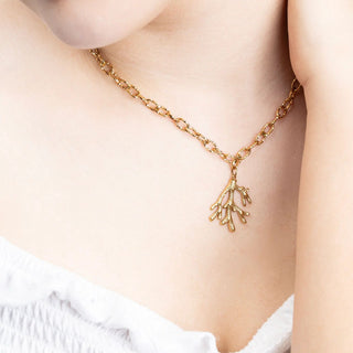 Gold chain necklace with a coral-like pendant worn by a person.