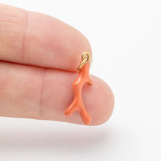 coral-shaped earring held between fingers on a white background