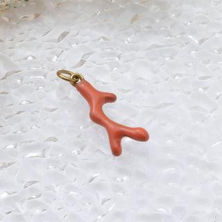 Coral-colored branch-shaped pendant on a gold chain against a textured white background