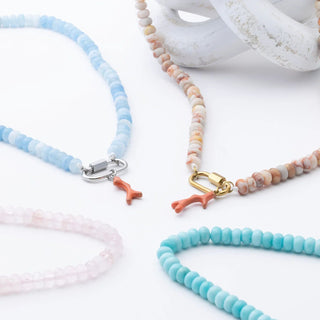 Set of beaded necklaces with coral charms on a white surface