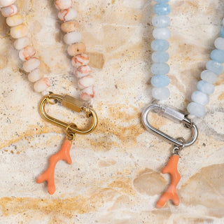 Two beaded necklaces with coral charm pendants on a textured beige surface.