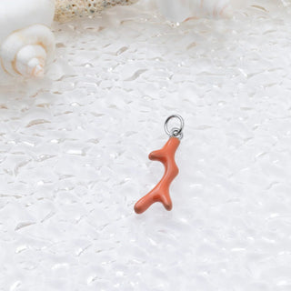 Coral branch charm on a textured white surface with shells in the background