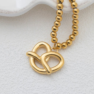 Gold beaded necklace with a pretzel pendant on a white background