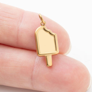 Gold popsicle pendant held between fingers on a light background