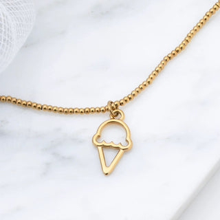 Gold ice cream cone necklace on a marble surface