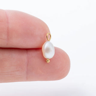 Pearl earring with gold hook on a finger against a white background