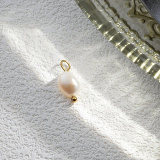 Pearl charm with gold loop on a textured white surface