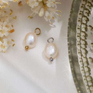 Two pearl charms on a white fabric background with flowers and a decorative object.