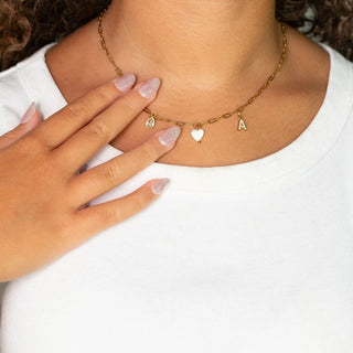 Gold necklace with heart and letter 'A' charms worn by a person with a white shirt.