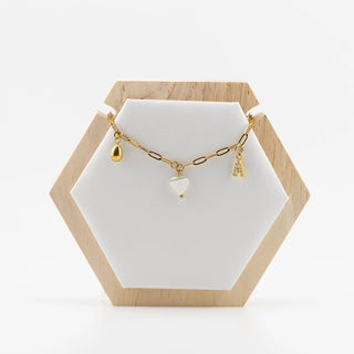 Gold necklace with charms on a white stand with a wooden hexagonal base