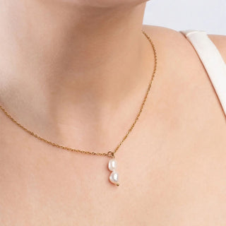 Gold necklace with a pearl pendant on a person wearing a white top.
