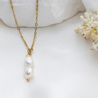 Gold necklace with pearl pendant on a white surface with flowers