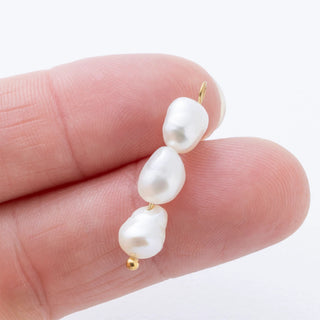 Pearl charm held between fingers on a white background