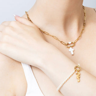 Gold chain necklace with a cross pendant and a bracelet with a seahorse charm on a person's wrist.