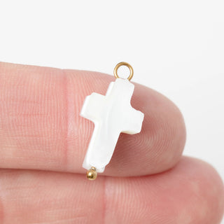 White cross pendant with gold accents held between fingers on a white background