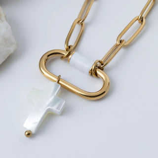 Gold chain necklace with a cross-shaped clasp and white pendant on a light background
