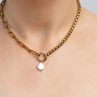 Gold chain necklace with a pearl pendant on a person's neck against a neutral background