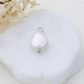 Silver baroque-shaped pendant on a white shell with flowers in the background