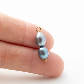 Two black pearls on gold clasps held between fingers against a white background