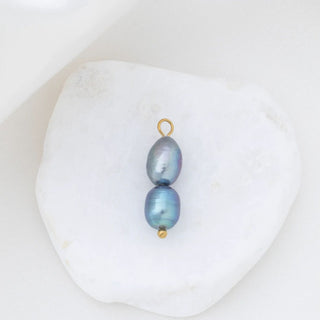 Two black pearls with gold clasps on a white shell