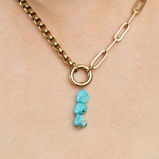 Gold necklace with turquoise pendant on a beige background