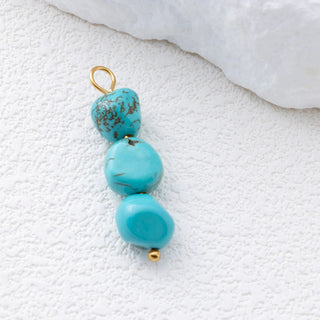 Turquoise bead pendant with gold accents on a textured white surface