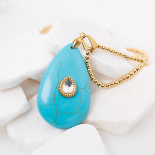 Turquoise teardrop pendant with gold chain on a white background