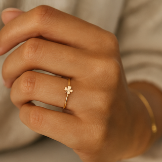Close-up of a hand wearing a gold ring with a clover design on a neutral background