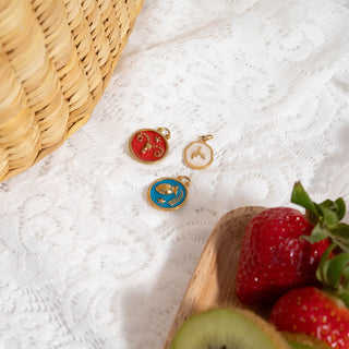 Three colorful charms on a white textured surface with strawberries and kiwis.