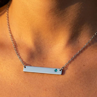 Necklace with a bar pendant and green gemstone on a person's neck