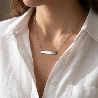 Silver necklace with a bar pendant worn by a person in a white shirt.