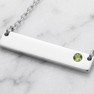 Silver bar necklace with a green gemstone on a marble surface